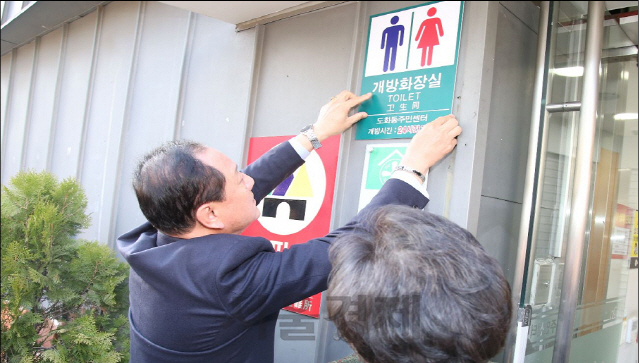 유동균(왼쪽) 마포구청장이 지난해 11월 서울시 마포구의 한 주민센터에 24시간 개방화장실 표지판을 부착하고 있다./사진제공=마포구청