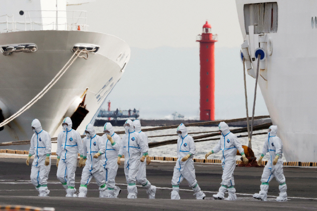7일(현지시간) 일본 요코하마항에 정박한 대형 크루즈선 ‘다이아몬드프린세스’호 앞을 방호복과 보호안경을 착용한 의료진이 지나가고 있다.  /요코하마=로이터연합뉴스