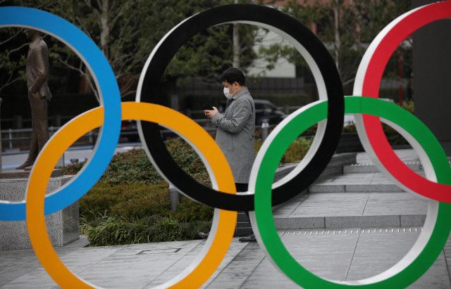 A man wearing protective face mask, following the outbreak of the coronavirus, looks at his mobile phone next to The Olympic rings in front of the Japan Olympics Museum in Tokyo, Japan, March 4, 2020. REUTERS/Stoyan Nenov        <저작권자(c) 연합뉴스, 무단 전재-재배포 금지>