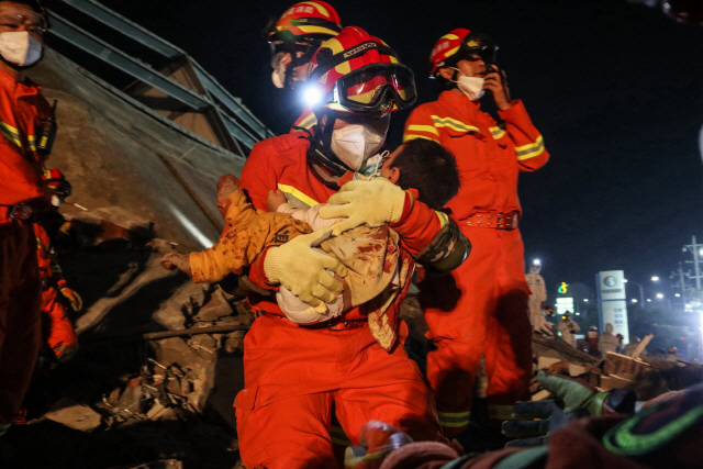 30여명이 매몰된 것으로 추정되는 가운데 다음날 새벽 구조대가 무너진 건물에서 남자아이를 구출해내고 있다(작은 사진).  /취안저우=AFP연합뉴스