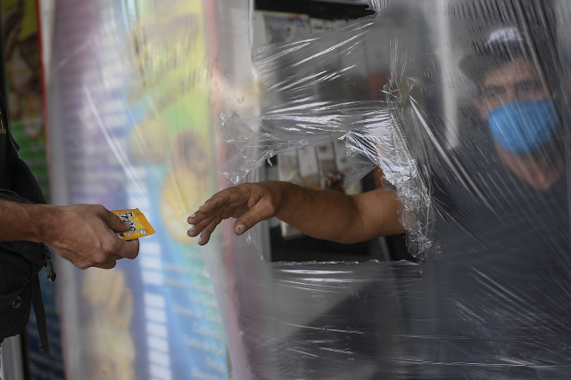베네수엘라 카라카스의 한 상점에서 29일(현지시간) 계산대 직원이 코로나19 예방을 위해 비닐 가림막 너머로 물건을 받고 있다. /카라카스=AP연합뉴스