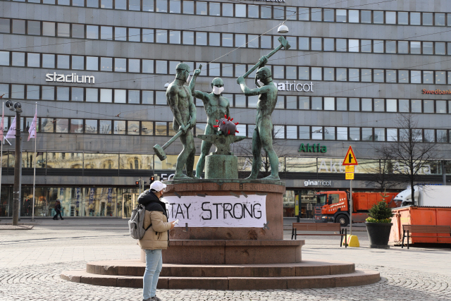 지난달 31일(현지시간) 핀란드 헬싱키에서 한 시민이 마스크를 쓴 ‘세 명의 대장장이’ 동상 앞을 지나고 있다. /헬싱키=신화연합뉴스