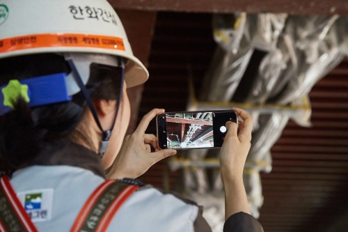 <한화건설 직원이 건설현장에서 휴대폰 앱을 활용해 안전관리를 하고 있다><o:p></o:p>