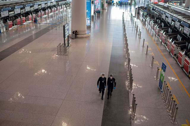 중국 베이징의 서우두국제공항 터미널이 13일 코로나19의 여파로 한산한 가운데 샤워캡과 비닐장갑을 착용한 공항 보안요원들이 터미널 안을 순찰하고 있다. /베이징=AFP연합뉴스