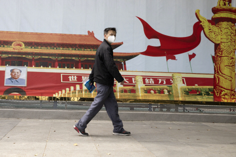 지난 16일(현지시간) 중국 후베이성 우한 도심에서 마스크를 쓴 남성이 톈안먼 사진이 걸린 정부 선전 포스터 앞을 지나고 있다.   /우한=AP연합뉴스
