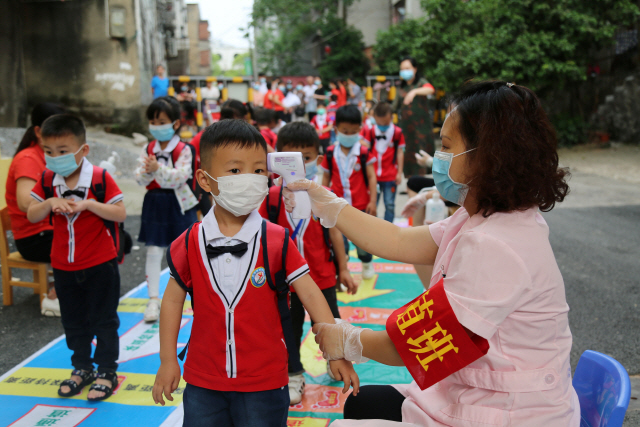 중국 각지에서 코로나19로 문을 닫았던 학교와 유치원들이 잇따라 수업을 재개한 가운데 후난성 남부 융저우의 한 유치원에서 11일(현지시간) 직원이 등원하는 유치원생의 체온을 재고 있다.  /융저우=로이터연합뉴스