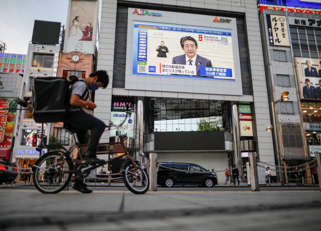 지난 14일 일본 도쿄 신주쿠의 한 건물에 설치된 대형 스크린을 통해 아베 신조 일본 총리의 코로나19 대응 관련 기자회견이 방송되고 있다./도쿄=로이터연합뉴스