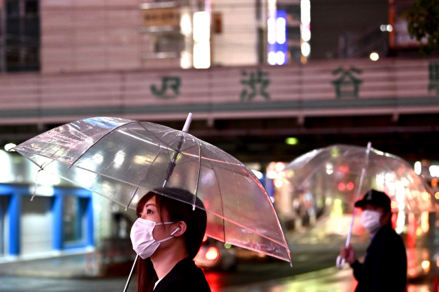 19일 일본 도쿄에서 마스크를 착용한 여성이 우산을 쓴 채 길을 걷고 있다. /도쿄=AFP연합뉴스