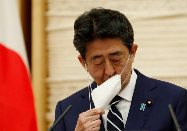 아베 신조 일본 총리가 25일 열린 기자회견을 시작하며 마스크를 벗고 있다. 일본 정부는 이날 코로나19 관련 한국인에 대한 무비자 입국 제도의 효력정지를 한 달 연장하기로 했다. /도쿄=AFP연합뉴스