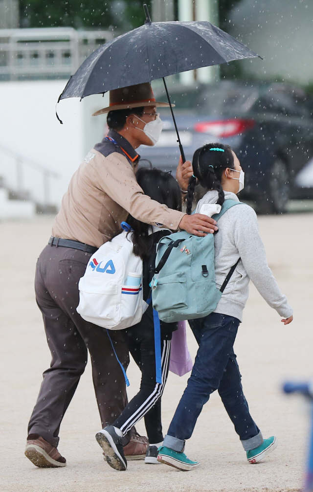 갑작스럽게 소나기가 내린 28일 오전 서울 종로의 한 초등학교에서 학교보안관이 우산을 미처 준비하지 못한 아이들에게 우산을 씌워주며 교실로 함께 이동하고 있다. /연합뉴스