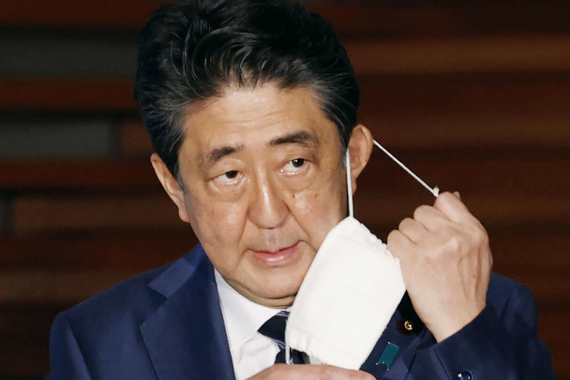 아베 신조 일본 총리가 21일 도쿄에서 기자회견에 앞서 마스크를 벗고 있다. /AP연합뉴스