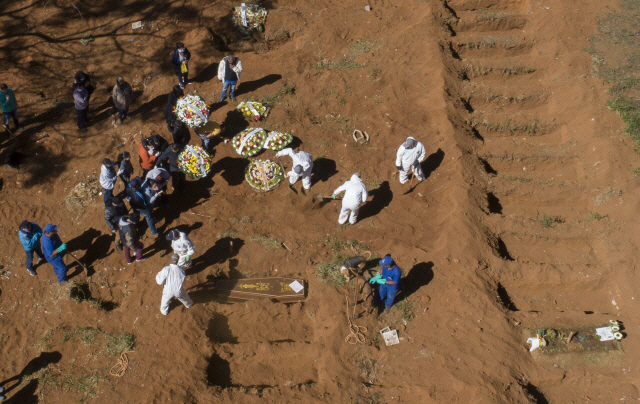 지난 28일(현지시간) 브라질 상파울루주의 빌라포르모사 공동묘지에서 보호장구를 착용한 관계자들이 코로나19로 사망한 희생자의 관을 묻고 있다./AP연합뉴스