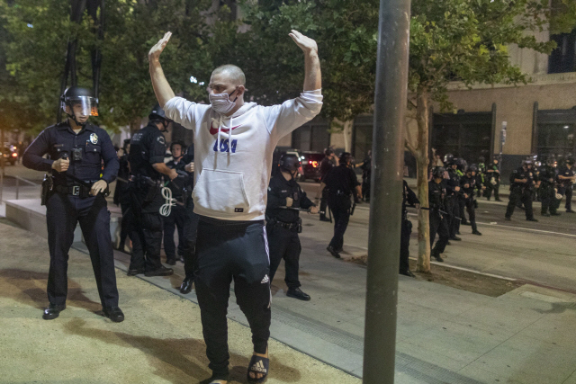 6일(현지시간) 미국 로스앤젤레스(LA)에서 마스크를 쓴 한 시위자가 경찰을 뒤에 두고 손을 번쩍 들고 있다./AFP연합뉴스