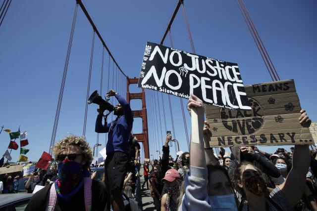 6일(현지시간) 미국 캘리포니아주 샌프란시스코의 금문교 위에서 흑인 남성 조지 플로이드 사망 사건에 항의하는 시위대가 ‘정의 없이 평화 없다’라고 적힌 손팻말을 들고 행진하고 있다./AP연합뉴스