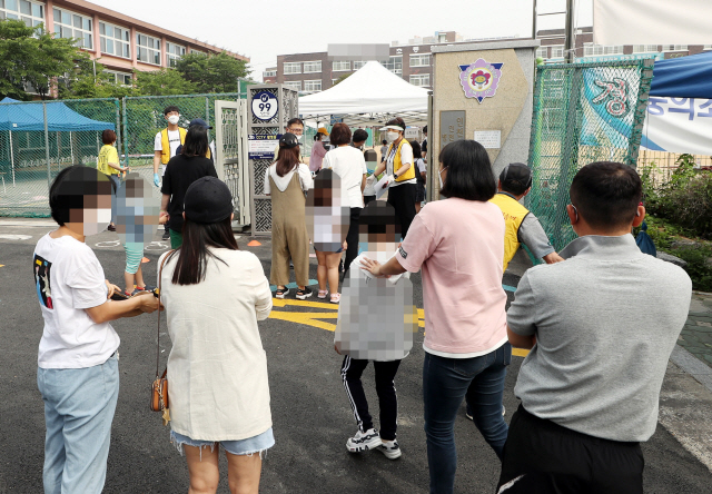 인천지역에 신종 코로나바이러스 감염증(코로나19) 확진자가 속출한 17일 오전 확진자가 나온 인천시 미추홀구 한 초등학교 정문에 검체 검사를 받으러 온 학생들이 부모와 함께 줄지어 서 있다. /연합뉴스