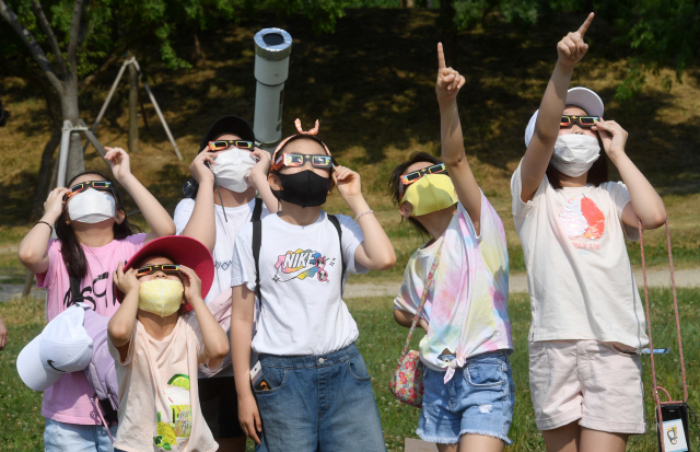 태양 관측용 특수안경을 쓴 어린이들이 21일 오후 서울 여의도 한강공원에서 부분 일식을 관찰하며 하늘을 가리키고 있다. 우리나라에서 관찰할 수 있는 다음 부분일식은 10년 뒤인 2030년 6월 1일 발생한다./권욱기자