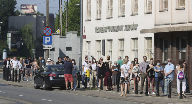 폴란드 대통령 선거가 실시된 28일(현지시간) 수도 바르샤바에서 시민들이 투표소로 들어가기 위해 마스크를 쓴 채 줄지어 기다리고 있다. 애초 지난 10일 치러질 예정이었다 코로나19 사태로 연기된 폴란드 대선은 이날 코로나19 확산 우려에도 불구하고 사회적 거리두기를 준수하며 예정대로 진행됐다.  /AP연합뉴스