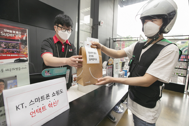 KT 대리점 직원이 부릉 라이더에게 ‘1시간배송’ 서비스를 위해 스마트폰을 건네고 있다./사진제공=KT