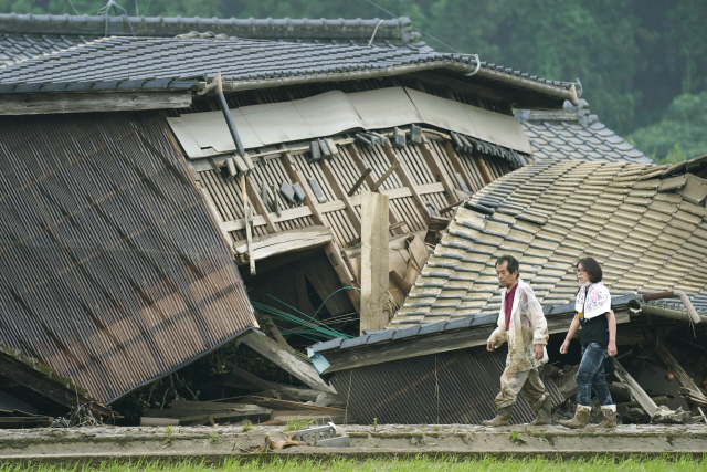 5일 일본 구마모토현 구마마을에서 한 부부가 전날 새벽부터 내린 폭우로 무너진 주택 앞을 지나가고 있다.  /AP연합뉴스