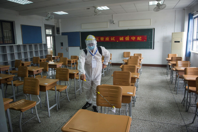 5일(현지시간) 중국 우한의 한 학교에서 보호장구를 착용한 관계자가 교실의 책상과 의자를 소독하고 있다./AFP연합뉴스