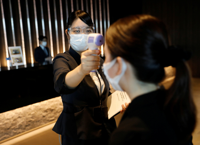 26일 일본 도쿄의 한 호텔에서 직원이 한 고객의 발열 여부를 체크하고 있다./로이터연합뉴스