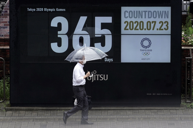 23일 일본 도쿄에서 마스크를 착용한 남성이 도쿄 올림픽이 365일 남았음을 알려주는 달력 앞을 지나가고 있다. /AP연합뉴스