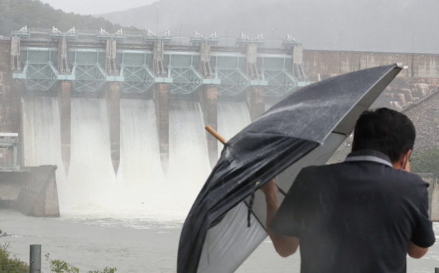 전국적으로 강한 비가 하루 종일 내린 지난 23일 오후 우산을 쓴 한 시민이 충북 청주시 대청댐에서 방류된 물이 흘러나오는 모습을 카메라에 담고 있다. /청주=연합뉴스