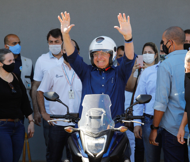 자이르 보우소나루 브라질 대통령이 25일(현지시간) 코로나19 검사에서 음성 판정을 받았다고 밝힌 뒤 오토바이를 타고 외출하며 두 팔을 치켜들고 있다./AFP연합뉴스