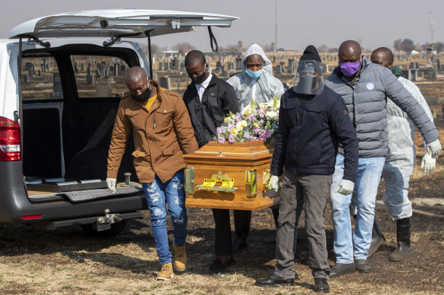 지난 23일(현지시간) 남아프리카공화국 요하네스버그의 동쪽에 위치한 토코자에서 마스크와 장갑 등 보호장구를 착용한 사람들이 코로나19로 사망한 시신이 담긴 관을 옮기고 있다./AP연합뉴스