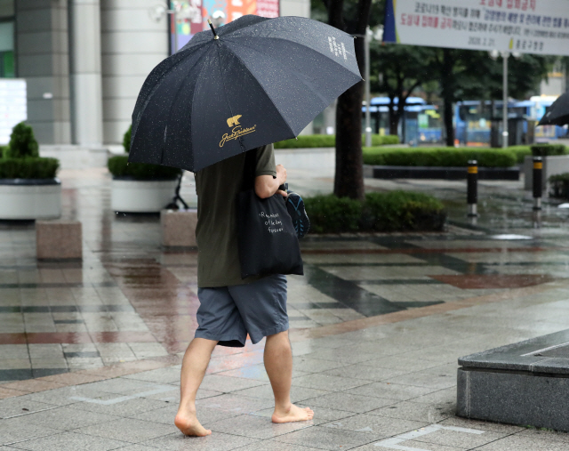 1일 정오경 서울 시내에 강한 빗줄기가 쏟아지자 한 시민이 신발을 벗고 맨발로 이동하고 있다./연합뉴스