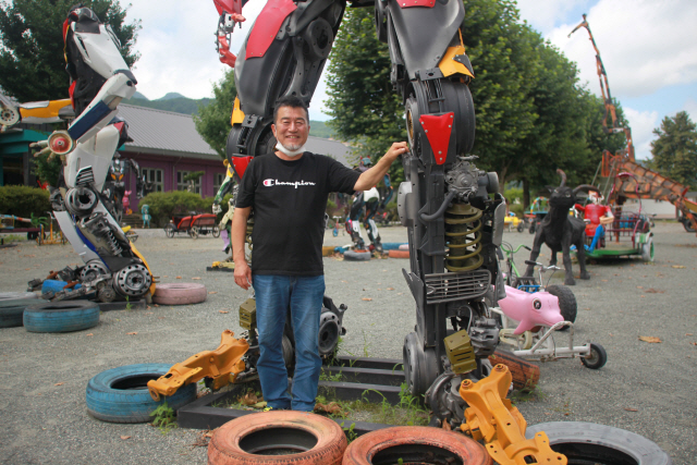 오대호 작가가 폐차로 만든 로봇작품 앞에서 환하게 웃고 있다. 6m 높이의 작품에는 자동차 1대 이상의 부품이 들어갔다.