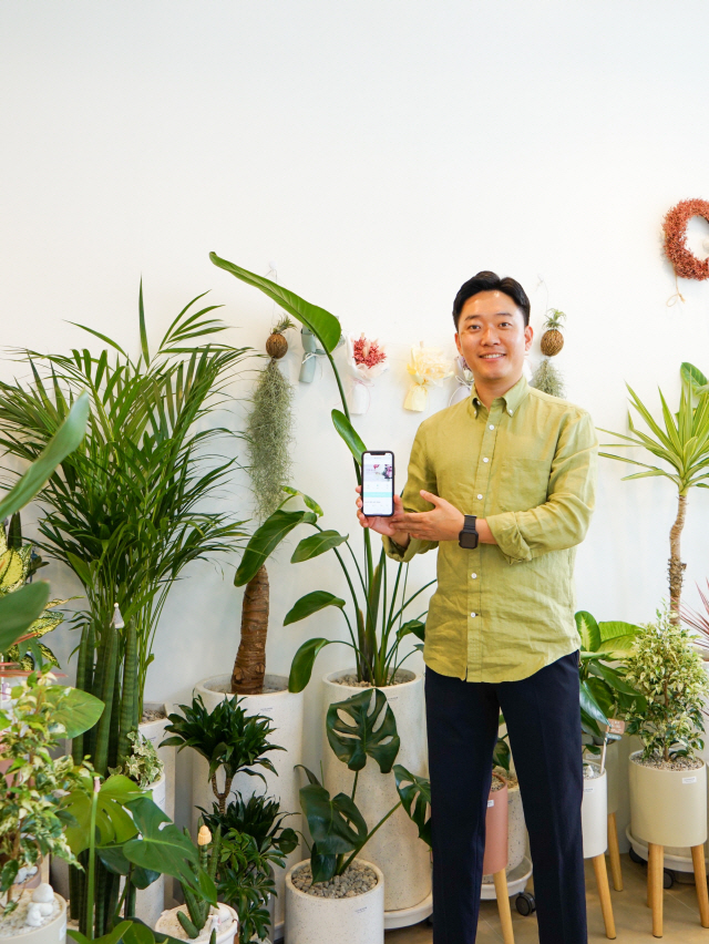 박명환 플디 대표가 꽃과 식물로 둘러싸인 본사 사무실에서 플디 애플리케이션 화면을 들어보이고 있다. /사진제공=플디