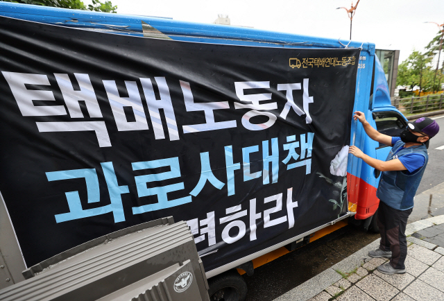 지난 7일 서울 여의도 국회 앞에서 열린 ‘전국 동시 택배차량 추모행진’에서 한 참석자가 택배 차량에 관련 대형 현수막을 부착하고 있다./연합뉴스