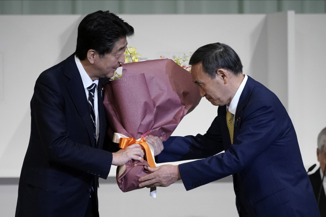 ‘상왕’의 축하?  14일 일본 도쿄에서 열린 자민당 총재선거에서 압도적 표차로 당선된 스가 요시히데(오른쪽) 관방장관이 아베 신조 총리로부터 꽃다발을 받고 있다.   /EPA연합뉴스