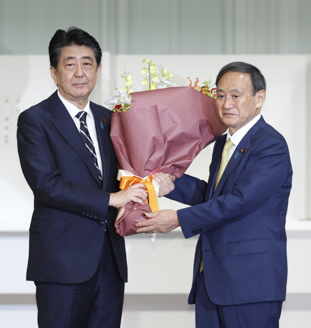 아베 신조(安倍晋三) 일본 전 총리가 지난 14일 도쿄 한 호텔에서 열린 집권 자민당 총재 선거에서 당선된 스가 요시히데(菅義偉) 신임 총리에게 꽃다발을 건네고 있다./연합뉴스