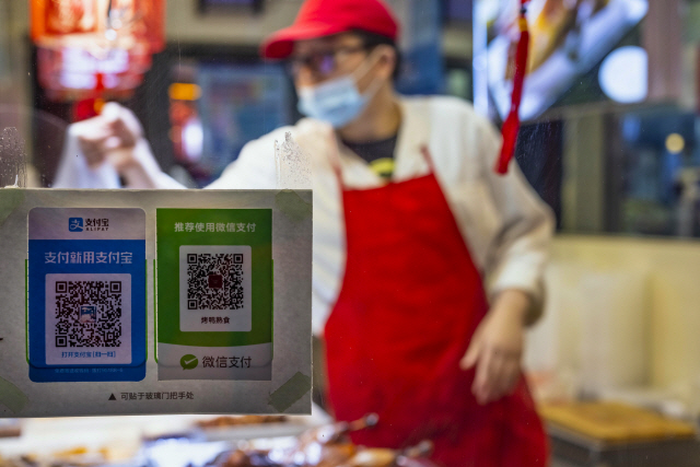 중국 상하이의 한 상점 주인이 마스크를 쓰고 고객에게 상품을 건제고 있다. 창문에는 알리페이이와 위챗페이먼트 QR코드가 붙어 있다. /EPA연합뉴스