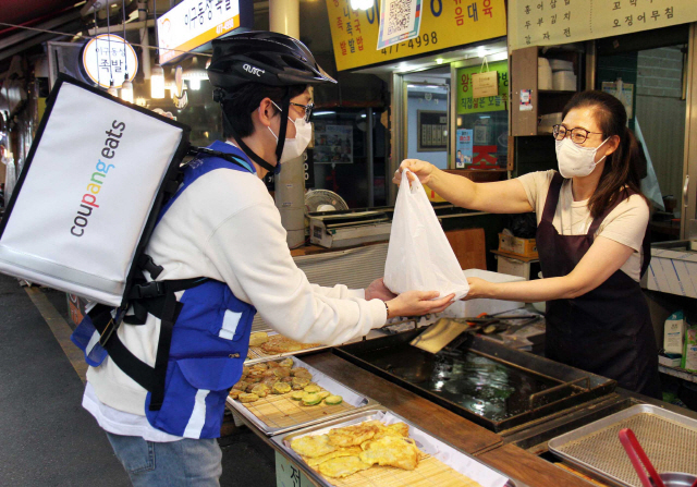 쿠팡이츠 배달 라이더가 서울 한 전통시장의 식당에서 고객이 주문한 상품을 받고 있다.