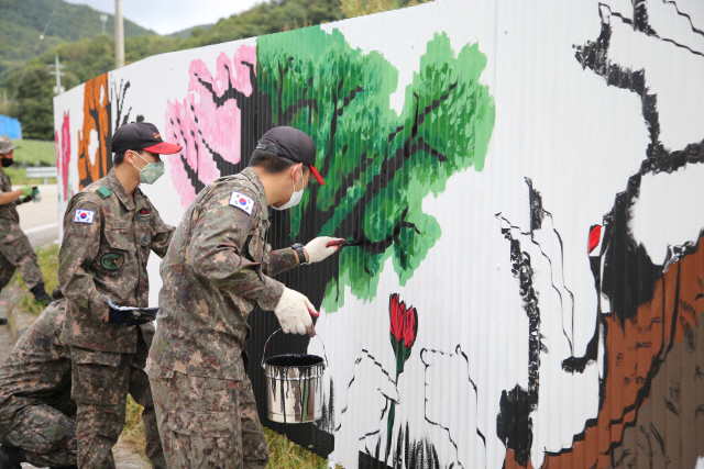 육군 과학화전투훈련단(KCTC) 장병들이 8일 강원도 인제군 남면 정자리마을과 접해 있는 훈련장 울타리에 벽화를 그려넣고 있다. KCTC는 훈련장과의 경계를 쉽게 식별할 수 있도록 50ｍ의 울타리를 설치했다고 밝혔다. /사진제공=육군 과학화전투훈련단