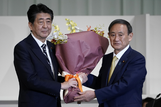 지난달 14일 아베 신조(왼쪽) 전 일본 총리가 후임으로 선정된 스가 요시히데 일본 총리에게 꽃다발을 건네고 있다./AP연합뉴스