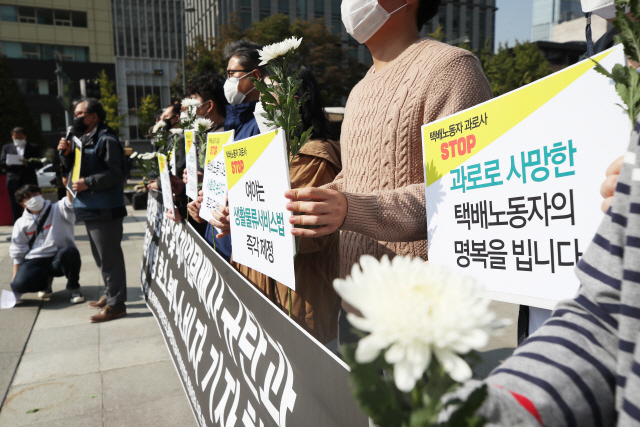 지난 19일 오후 서울 광화문광장 이순신 동상 앞에서 열린 ‘대기업 택배사 규탄과 택배노동자 과로사 예방 호소하는 택배 소비자 기자회견’에서 참석자들이 손팻말과 국화를 들고 있다.   /연합뉴스