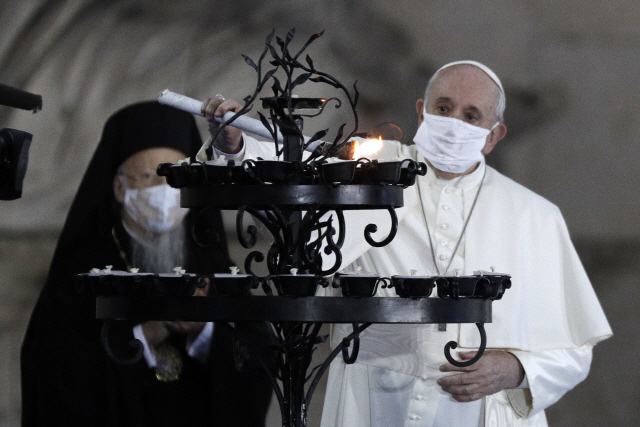 20일(현지시간) 마스크를 쓴 프란치스코 교황이 이탈리아 로마의 산타마리아 인 아라코엘라 성당에서 열린 세계 평화를 위한 종교 간 합동 기도회에 참석해 초에 불을 붙이고 있다. 교황의 경호를 담당하는 근위대원 중 최소 11명이 코로나19 확진 판정을 받자 교황은 이날 처음으로 마스크를 쓴 채 대중행사에 참석했다./AP연합뉴스