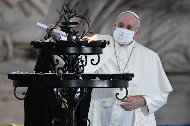 20일(현지시간) 마스크를 쓴 프란치스코 교황이 이탈리아 로마의 산타마리아 인 아라코엘라 성당에서 열린 세계 평화를 위한 종교 간 합동 기도회에 참석해 초에 불을 붙이고 있다. 교황의 경호를 담당하는 근위대원 중 최소 11명이 코로나19 확진 판정을 받자 교황은 이날 처음으로 마스크를 쓴 채 대중행사에 참석했다./EPA연합뉴스