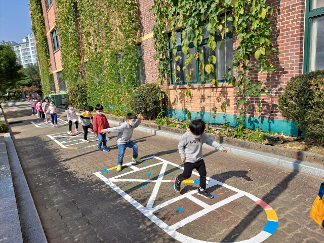 유치원 어린이들이 거리 두기를하며 바닥 그림을 활용해 즐겁게 놀고 있다.