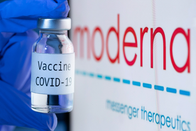 미국 제약회사 모더나의 로고를 배경으로 코로나19 백신이라고 표시된 약병을 연구원이 들고 있다. /APF연합뉴스