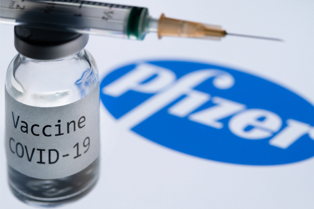 (FILES) In this file photo illustration taken on November 23, 2020, shows a syringe and a bottle reading “Covid-19 Vaccine” next to the Pfizer company logo. - The World Health Organization warned that vaccines were no magic bullet for the coronavirus crisis, as Russia started vaccinating its high-risk workers Saturday and other countries geared up for similar programmes. (Photo by JOEL SAGET / AFP)        <저작권자(c) 연합뉴스, 무단 전재-재배포 금지>
