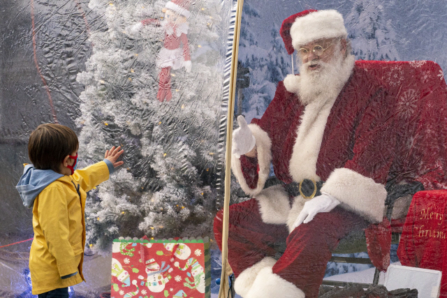 6일(현지 시간) 미국 워싱턴주 시애틀에서 한 어린이가 사회적 거리 두기를 위해 스노볼 텐트 안에 있는 산타를 향해 손을 내밀고 있다./AFP연합뉴스