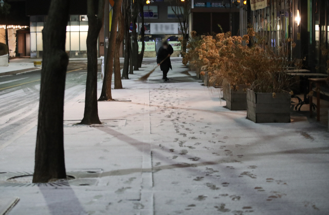밤사이 눈이 내린 18일 오전 서울 종로구 한 건물 앞에서 관계자들이 쌓인 눈을 쓸고 있다./연합뉴스