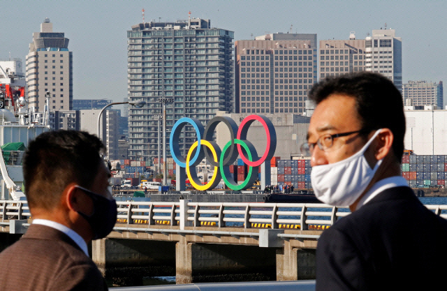 지난 1일(현지시간) 마스크를 쓴 사람들이 일본 도쿄 오다이바 해양공원에 올림픽을 상징하는 오륜 조형물이 다시 설치돼 있는 모습을 지켜보고 있다 이 조형물은 지난 8월 보수작업을 위해 일시 철거된 바 있다./로이터연합뉴스