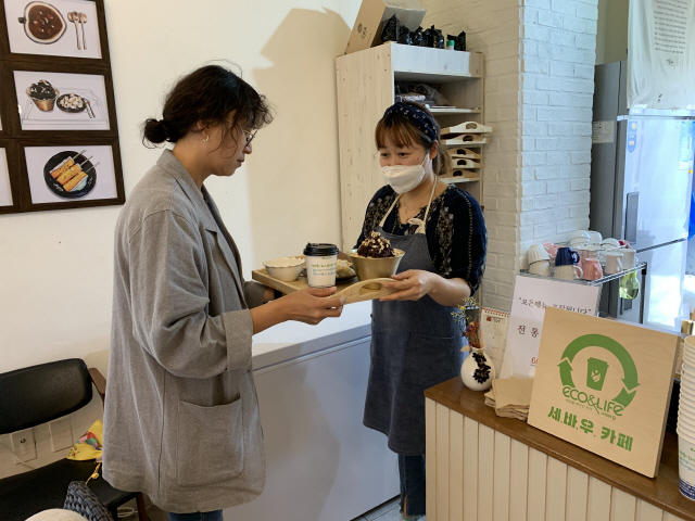 서울경제가 제주 올레길서 2년째 진행하고 있는 친환경 캠페인 ‘세상을 바꾸는 우리’에 참여하고 있는 올레길 주변 카페 사장(오른쪽)이 21일 손님에게 100% 재생 가능한 재활용컵에 커피를 담아 건네고 있다.  /사진 제공=제주 올레재단