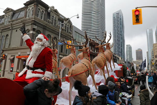 캐나다 토론토의 한 거리에서 20일(현지 시간) 마스크를 쓰지 않은 산타 복장의 남성이 역시 노마스크인 아이들 곁에서 손을 흔들고 있다. 이날 토론토에서는 코로나19 집합 제한에 반대하는 퍼레이드가 경찰의 불허에도 불구하고 진행됐다. /로이터연합뉴스